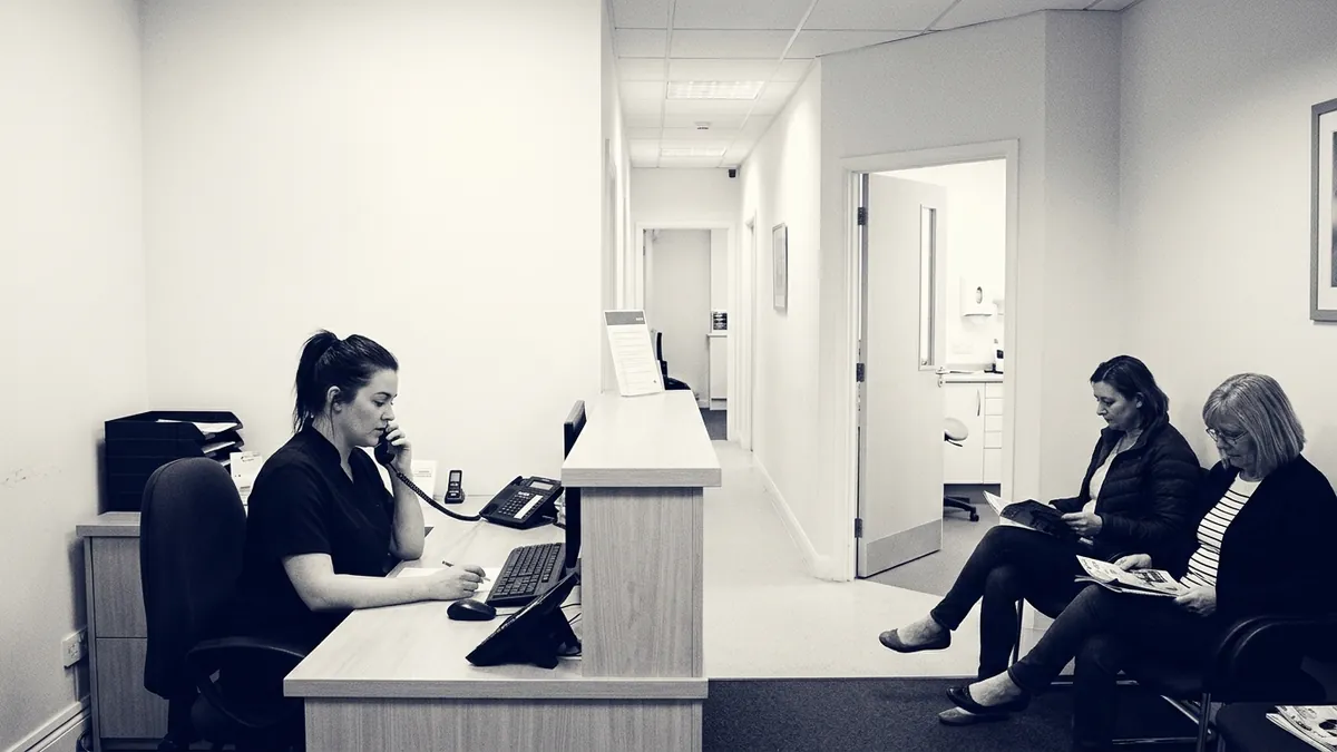 A dental receptionist answering the phone while patients wait in the corridor